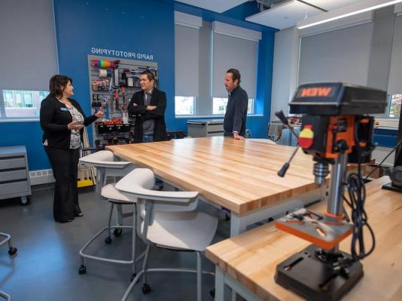 The new 研究、创新、设计、 和创业(RIDE)中心, 有木桌, 白色的椅子, 蓝色的墙, 以及贝弗里奇基金会的三位成员.