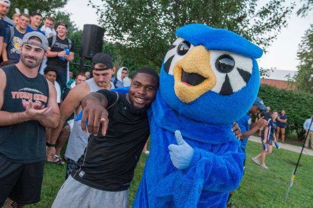 Nestor the Owl with his arm around a male student that the fall pep rally on the campus green