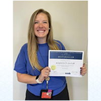 Kelsey Cottengim, an alumna of WSU, 穿着一件藏青色t恤，手里拿着一张纸，上面写着, 获得2023年马萨诸塞州杰出教育家奖的“认可证书”.